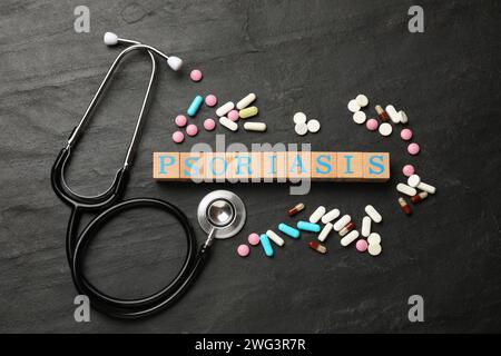 Word Psoriasis made of wooden cubes with letters, stethoscope and pills on dark gray textured table, flat lay Stock Photo