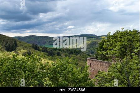 Sun shining on trees next to a wall near a castle on a hill above Bad Munster, Germany on a cloudy spring day. Stock Photo