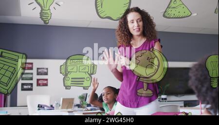 Image of green school icons over happy diverse pupils and female teacher talking in class Stock Photo