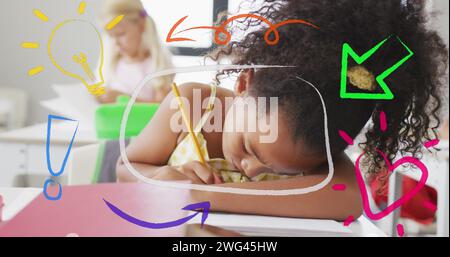 Image of colourful inspiration icons over busy biracial schoolgirl working in class Stock Photo