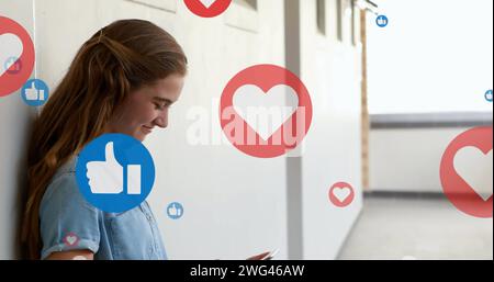 Heart and like icons floating against caucasian woman smiling while using smartphone Stock Photo