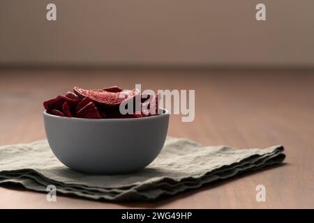 Beetroot chips in ceramic bowl on wooden table with linen napkin, shallow focus Stock Photo