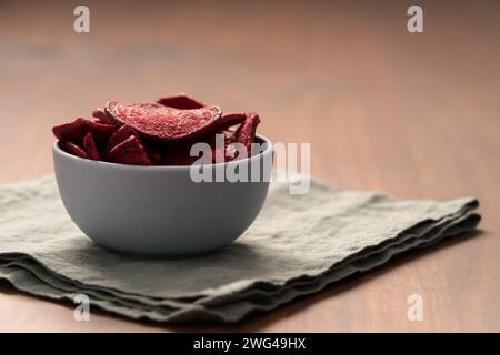 Beetroot chips in ceramic bowl on wooden table with linen napkin, shallow focus Stock Photo
