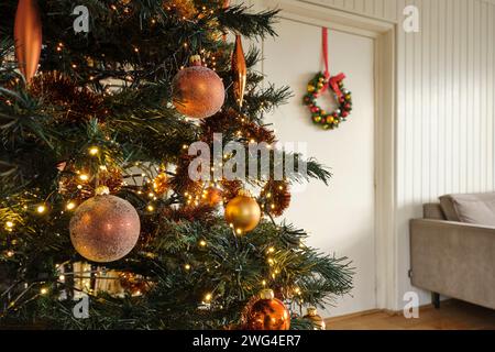 Christmas tree with golden balls in an interior and christmas wreath with red ribbon and decoration with golden, red and silver christmas balls. Stock Photo