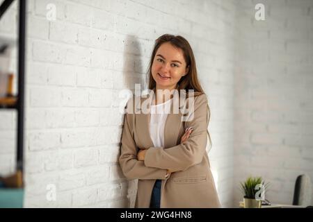 Happy Businesswoman in Office. Stylish Beautiful Manager Smiling It stands against a white brick wall, Working on Financial and Marketing Projects Stock Photo