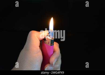 The fire and the included pink plastic lighter lie in a female hand on a black glossy surface. Stock Photo