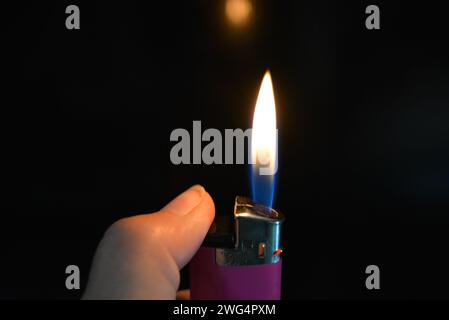 The fire and the included pink plastic lighter lie in a female hand on a black glossy surface. Stock Photo