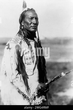 Big Mouth Spring, c1910. Big Mouth Spring, three-quarter length portrait, standing, facing right, braids, one feather, beaded buckskin shirt, decorated scalp lock on right shoulder, black silk neckerchief. Stock Photo