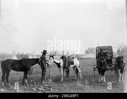 High Medicine Rock, Crow Indian with two horses at left, Her Horse Kills with child in buggy at right, tepees and circus type tent in background, Montana, c1908. Stock Photo