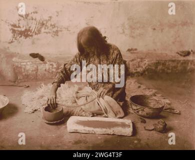 Zuni potter, c1903. Zuni woman kneeling on animal skin on floor, making pottery. Stock Photo