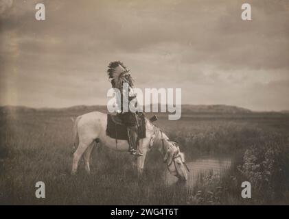 An oasis in the Badlands, c1905. Photograph shows Red Hawk, an Oglala warrior, sitting on a horse that is drinking from a small pond in the Badlands of North Dakota. Stock Photo