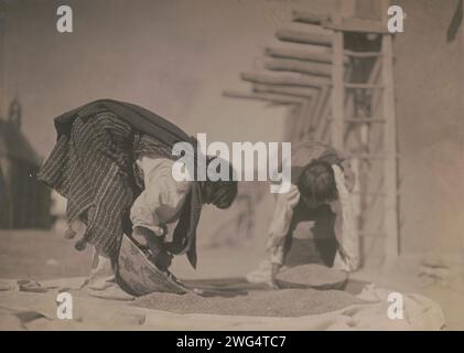 Cleaning wheat-San Juan, c1905. Two Tewa people processing wheat outside pueblo structure, San Juan Pueblo, New Mexico. Stock Photo