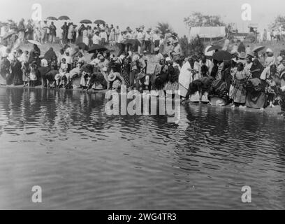 At the pool, animal dance-Cheyenne, c1927. Cheyenne people gathered along waterfront, some dipping hands in water, some carrying umbrellas. Stock Photo