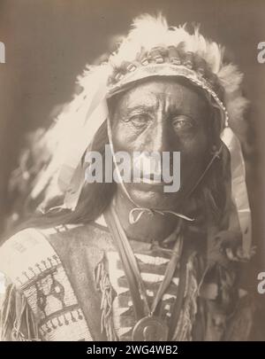 Jack Red Cloud, 1907. Photograph shows head-and-shoulders portrait of Jack Red Cloud, standing, wearing full headdress, traditional clothing, and medallion, facing front. Stock Photo