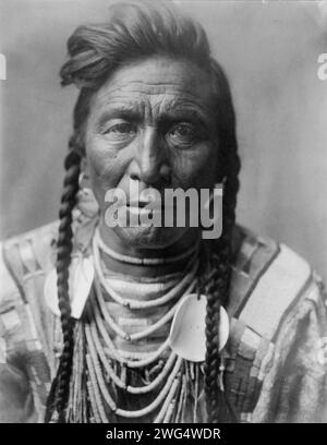 Strike On his Head, Crow Indian, Montana, head-and-shoulders portrait, facing front, loose forelock, braids, beaded buckskin shirt, beads and two large shell disks around neck, c1908. Stock Photo