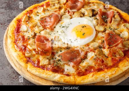 Bismark is the name of a traditional Italian pizza topped with tomato sauce, mozzarella, prosciutto, and egg closeup on the wooden board on the table. Stock Photo