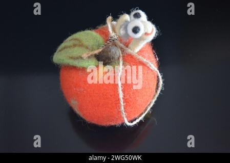 Soft Ukrainian toy made of natural wool and knocked down felt in the form of a bright ripe apple with a cheerful worm located on black matte surface. Stock Photo