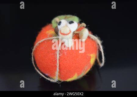 Soft Ukrainian toy made of natural wool and knocked down felt in the form of a bright ripe apple with a cheerful worm located on black matte surface. Stock Photo