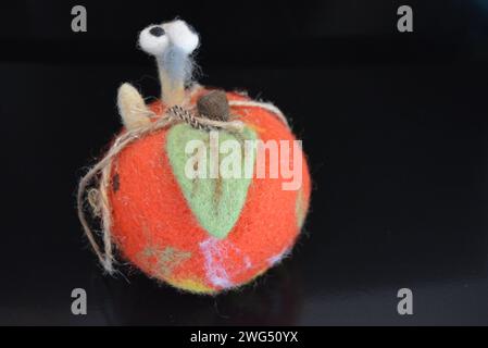 Soft Ukrainian toy made of natural wool and knocked down felt in the form of a bright ripe apple with a cheerful worm located on black matte surface. Stock Photo