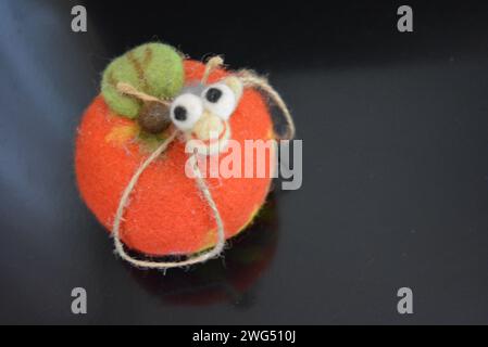 Soft Ukrainian toy made of natural wool and knocked down felt in the form of a bright ripe apple with a cheerful worm located on black matte surface. Stock Photo