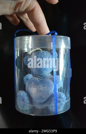 The blue teddy bear made of natural wax is made in the shape of a candle and packed in a plastic box with a blue bow on a black glossy background. Stock Photo