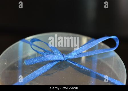 The blue teddy bear made of natural wax is made in the shape of a candle and packed in a plastic box with a blue bow on a black glossy background. Stock Photo