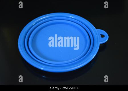 Blue folding and multifunctional rubber plate, a bowl with a plastic edging on a black glossy surface. Stock Photo