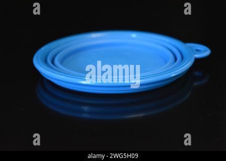 Blue folding and multifunctional rubber plate, a bowl with a plastic edging on a black glossy surface. Stock Photo