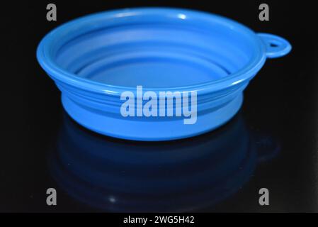 Blue folding and multifunctional rubber plate, a bowl with a plastic edging on a black glossy surface. Stock Photo