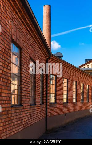 A well-preserved red brick industrial building, featuring a towering chimney against a bright blue sky, evokes a sense of historical significance. Stock Photo