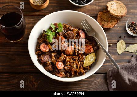 Stewed cabbage (polish bigos) with sauerkraut, mushrooms, smoked meats and spices in bowl over wooden background. Close up view Stock Photo