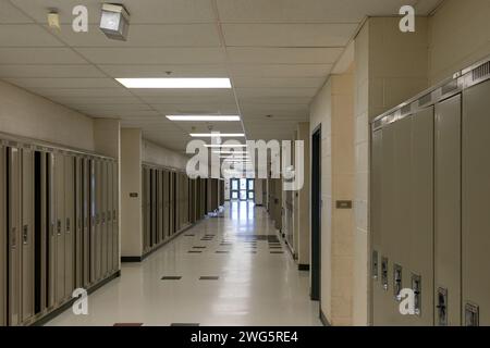 Empty school hallway - lined with closed lockers - beige walls - tiled floor - ceiling lights illuminating space - exit doors at the end. Taken in Tor Stock Photo
