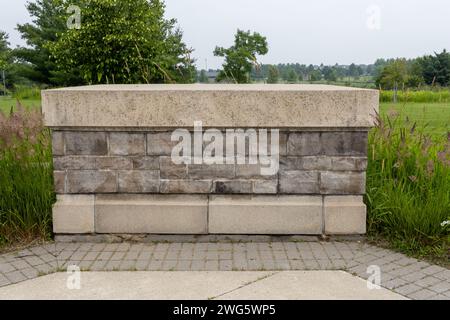 Blank stone wall sign - neutral tones - surrounded by greenery - outdoor setting - clear day. Taken in Toronto, Canada. Stock Photo