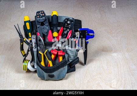 Electrician's bag with a professional electric tools. Pliers, wire cutters, strippers, screwdrivers, testers, crimping pliers. Plywood background. Pla Stock Photo