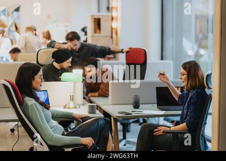 A focused group of three professionals engaging in discussion over a computer in a bustling creative office. Stock Photo