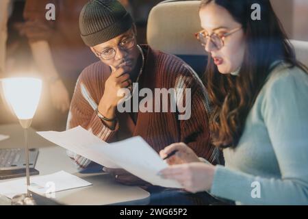 Two business professionals attentively discussing a project, with one holding a smart phone and documents in a well-lit office setting. Stock Photo