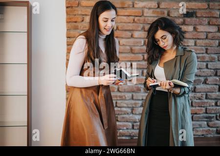 Two professional women collaborating and taking notes in a modern office environment. Stock Photo