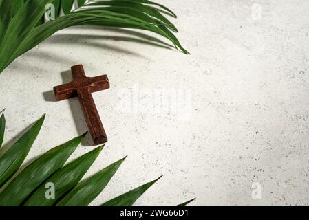 Palm Sunday. Wooden christian cross and palm leaves on white stone background, copy space. Palm sunday holiday concept. Stock Photo