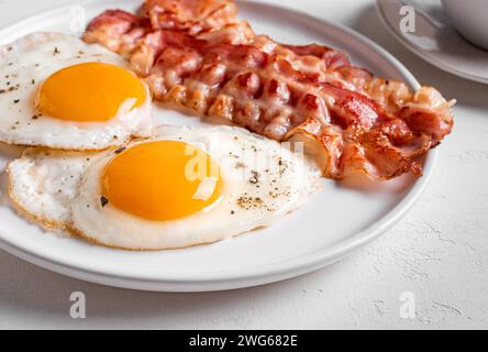 Breakfast with fried eggs and bacon close up. Fried sunny side eggs with bacon on plate, healthy keto meal. Stock Photo