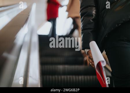 Close-up of a person riding an escalator holding a rolled document. Stock Photo