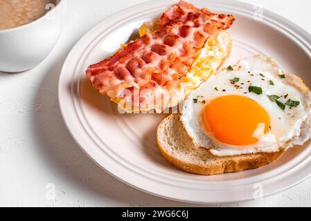 Breakfast sandwiches with fried egg, bacon, scrumbled egg close up and cup of coffee. Fried eggs with bacon on toasts and morning cappuccino coffee. Stock Photo