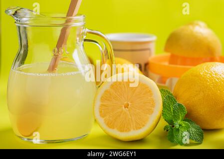 Pitcher of lemonade next to some lemons, mint, sugar jar and a manual juicer, close-up. Stock Photo