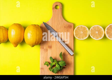 Cutting board with a knife and mint, with a row of whole lemons on one side and half lemons on the other. Stock Photo