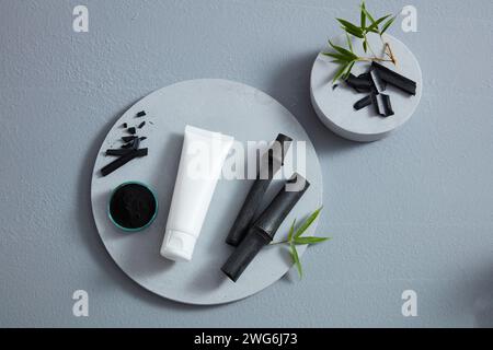 White cosmetic tube between an activated charcoal bowl and black bamboo, placed on big circle podium. Top view Stock Photo
