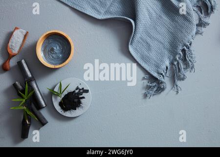 A bird's-eye view of charcoal powder, facial mask and towel on gray background. Text can be added in the blank space Stock Photo