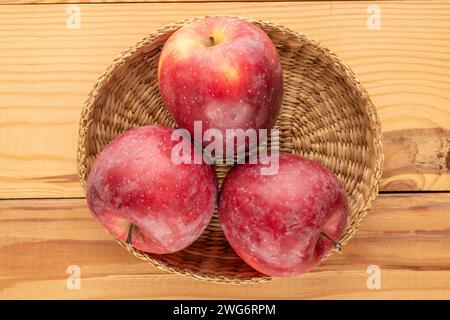 Three red apples in a straw plate on a wooden table, macro, top view. Stock Photo