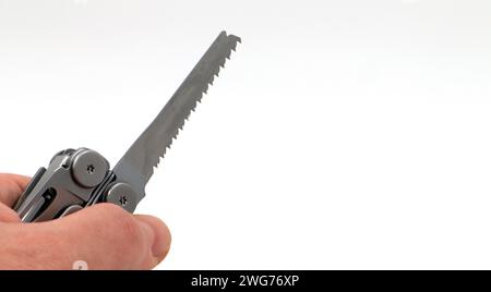 On a white background, a man's hand holds a steel multi-tool or pocket knife with an open saw. Compact and portable multi-tasking multitool with many Stock Photo
