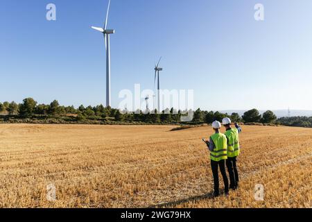 Team of engineers standing in the field inspecting the operation of wind turbines. Stock Photo
