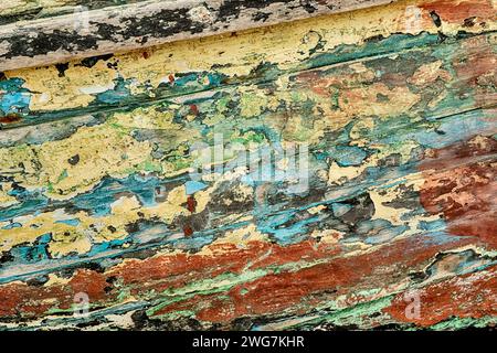 An abstract background is seen in the paint flakes peeling off the hull of a fishing boat painted with many different colors of paint. Stock Photo