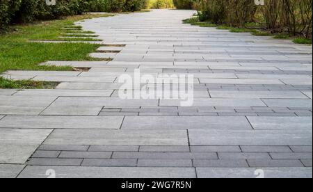Marble path paved with stone and square tiles. The pedestrian path is paved with paving stones. Grass grows between the tiles. Sidewalk in landscape g Stock Photo